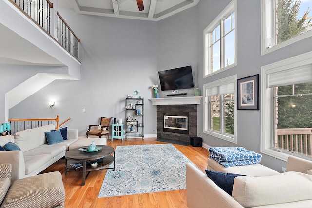 living room with a towering ceiling, light hardwood / wood-style floors, ceiling fan, and coffered ceiling