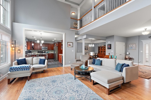 living room with decorative columns, light hardwood / wood-style floors, a healthy amount of sunlight, and a notable chandelier