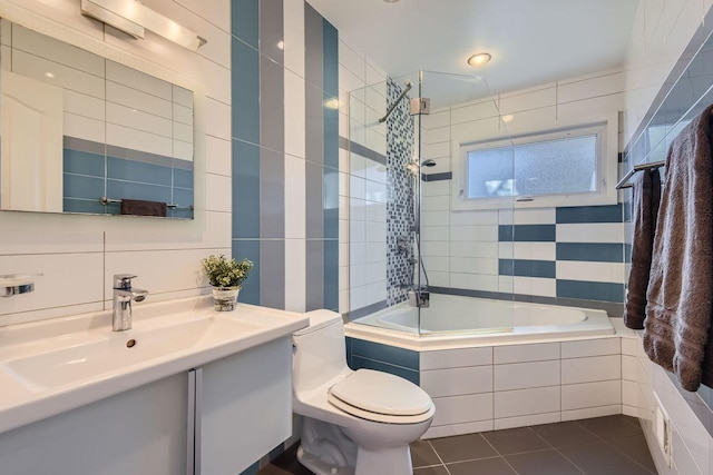 full bath featuring toilet, tile patterned floors, tiled shower / bath, vanity, and tile walls