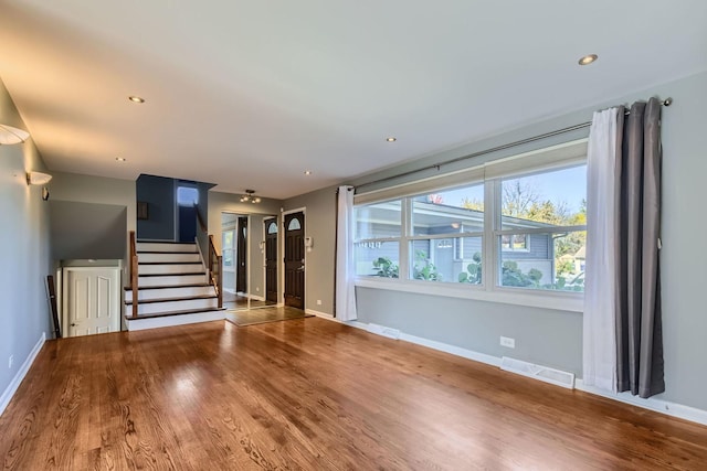 unfurnished living room featuring baseboards, stairs, visible vents, and wood finished floors