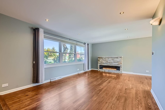 unfurnished living room with recessed lighting, visible vents, a stone fireplace, wood finished floors, and baseboards