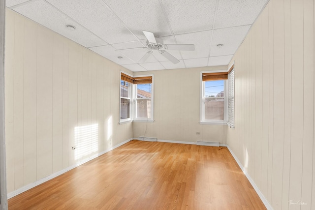 spare room featuring a drop ceiling, wood walls, and light wood-type flooring