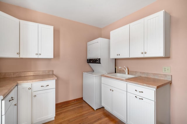 laundry room with cabinets, stacked washer and dryer, light hardwood / wood-style flooring, and sink