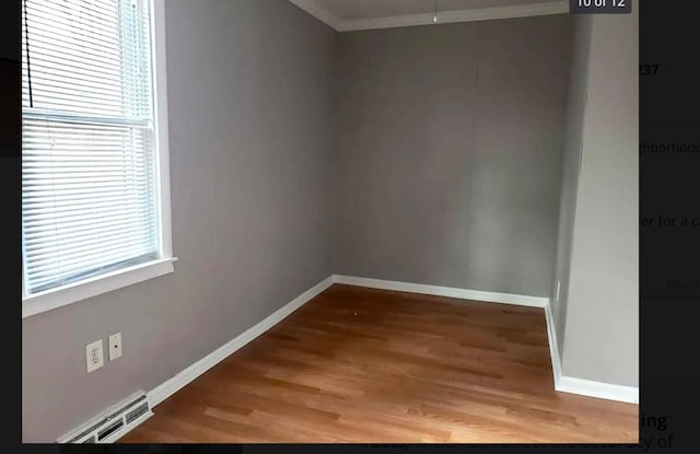 unfurnished room with wood-type flooring, crown molding, and a baseboard radiator