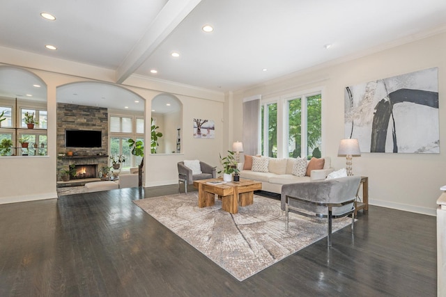 living room with beam ceiling, a stone fireplace, crown molding, and dark hardwood / wood-style floors