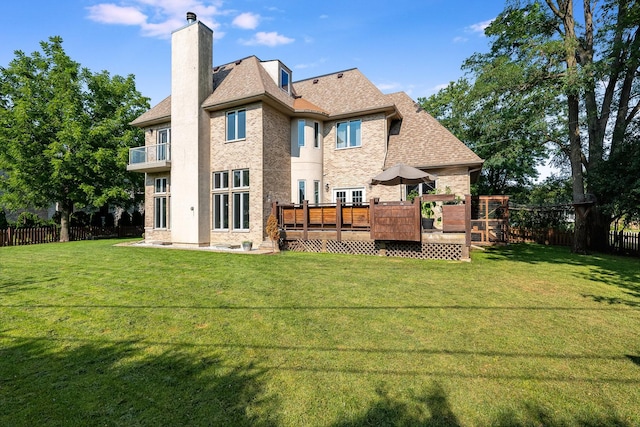 rear view of property featuring a yard, a balcony, and a wooden deck