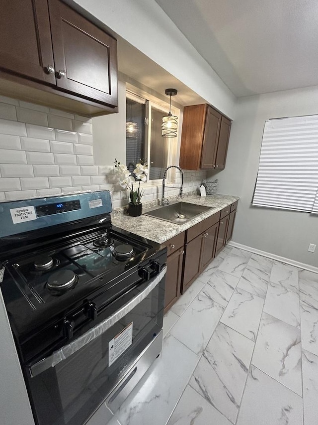 kitchen with gas stove, dark brown cabinetry, sink, hanging light fixtures, and tasteful backsplash