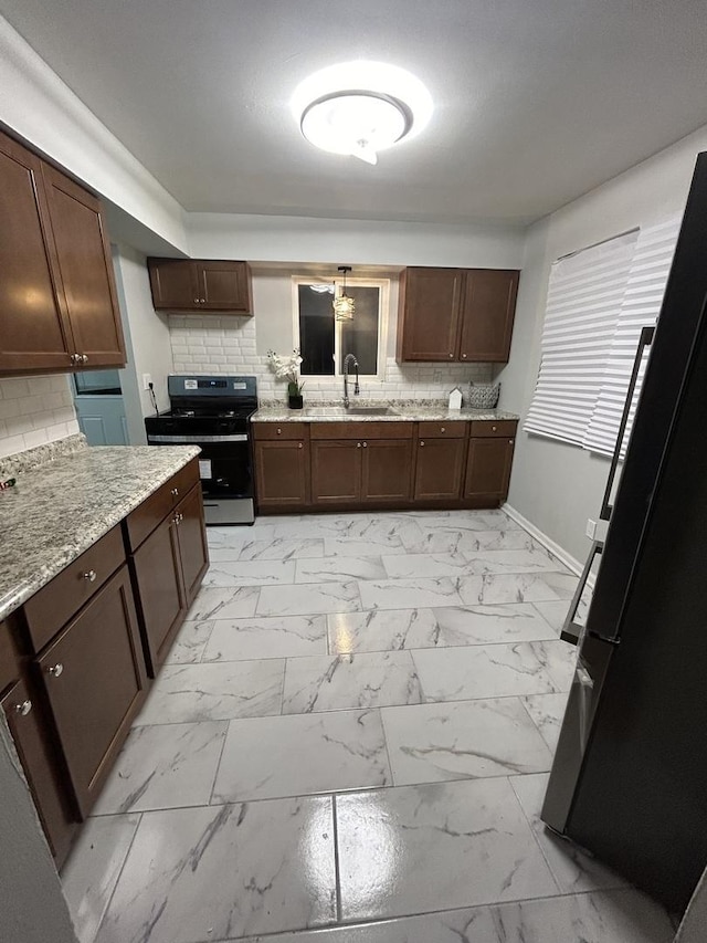 kitchen with stove, backsplash, sink, light stone counters, and dark brown cabinetry