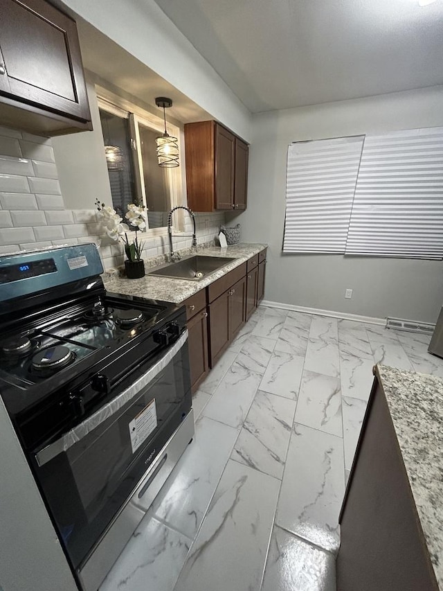 kitchen with sink, tasteful backsplash, light stone counters, pendant lighting, and stainless steel range with gas stovetop