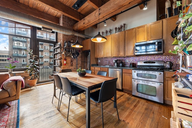 kitchen with appliances with stainless steel finishes, backsplash, pendant lighting, beamed ceiling, and hardwood / wood-style floors