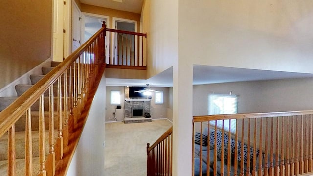 staircase with a high ceiling, carpet floors, a brick fireplace, and ceiling fan