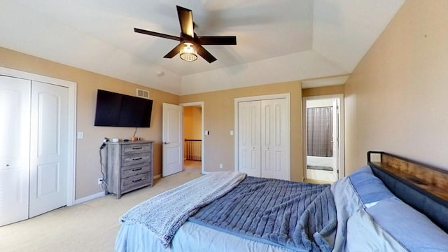 carpeted bedroom featuring multiple closets, ceiling fan, and ensuite bathroom