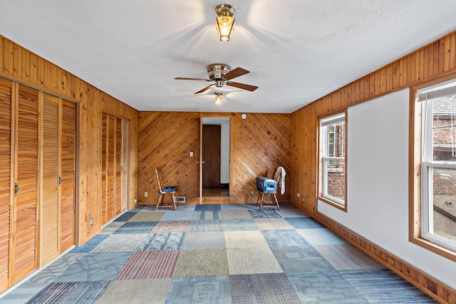 unfurnished room with carpet flooring, wooden walls, ceiling fan, and a textured ceiling