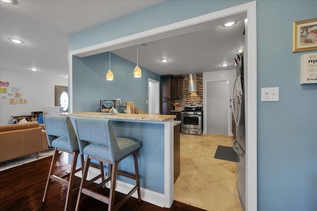 kitchen featuring a kitchen breakfast bar, kitchen peninsula, decorative light fixtures, dark brown cabinetry, and stainless steel appliances