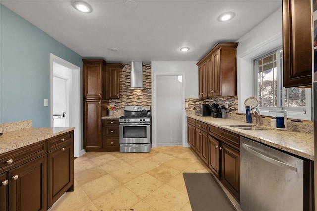 kitchen featuring decorative backsplash, light stone counters, wall chimney exhaust hood, stainless steel appliances, and sink