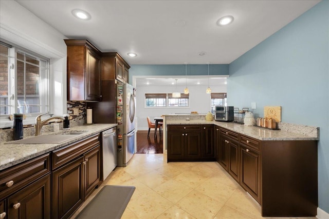 kitchen featuring dark brown cabinetry, sink, stainless steel appliances, hanging light fixtures, and kitchen peninsula