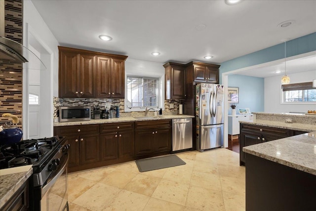 kitchen with decorative backsplash, appliances with stainless steel finishes, dark brown cabinets, sink, and decorative light fixtures