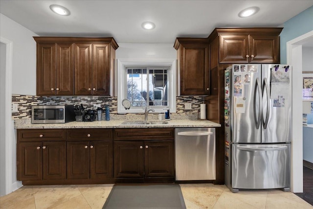 kitchen featuring appliances with stainless steel finishes, dark brown cabinetry, light stone counters, and sink