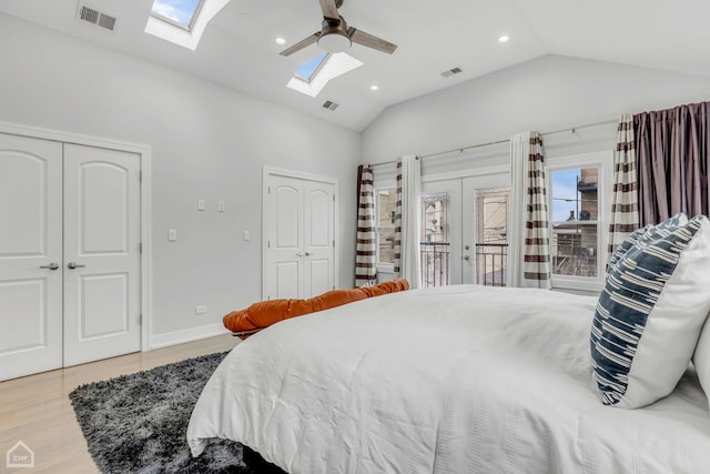 bedroom with ceiling fan, lofted ceiling with skylight, light hardwood / wood-style floors, french doors, and multiple closets