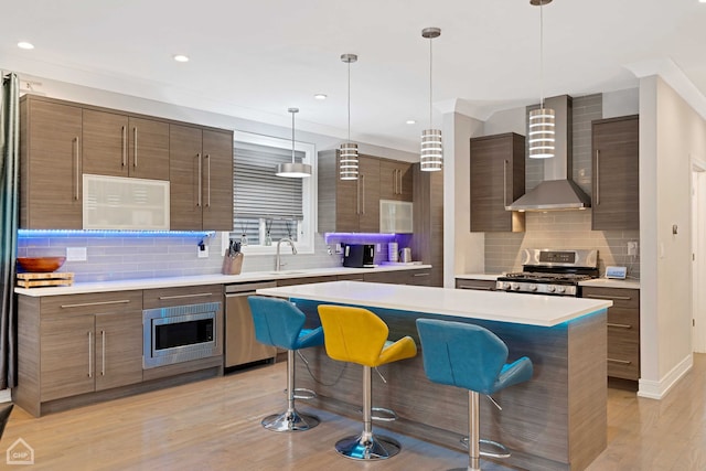 kitchen featuring pendant lighting, a kitchen breakfast bar, a center island, stainless steel appliances, and wall chimney exhaust hood