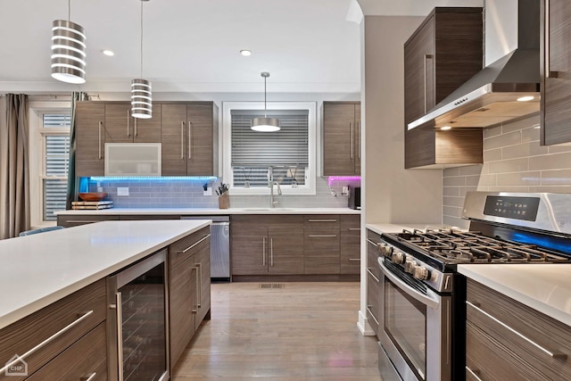 kitchen featuring wall chimney range hood, backsplash, stainless steel appliances, decorative light fixtures, and beverage cooler