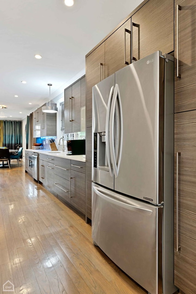 kitchen with hanging light fixtures, sink, stainless steel fridge, and light wood-type flooring