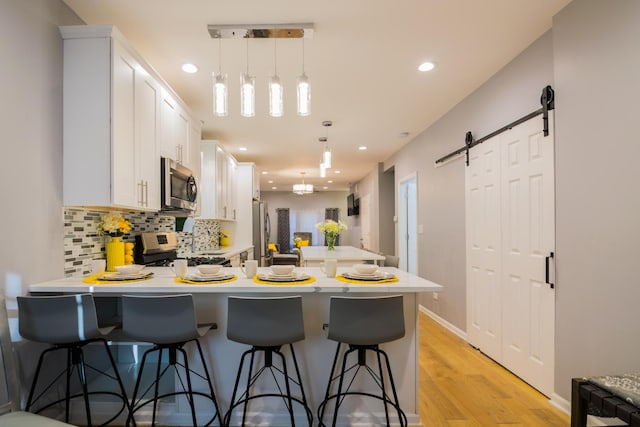 kitchen with a barn door, kitchen peninsula, a breakfast bar, white cabinets, and appliances with stainless steel finishes