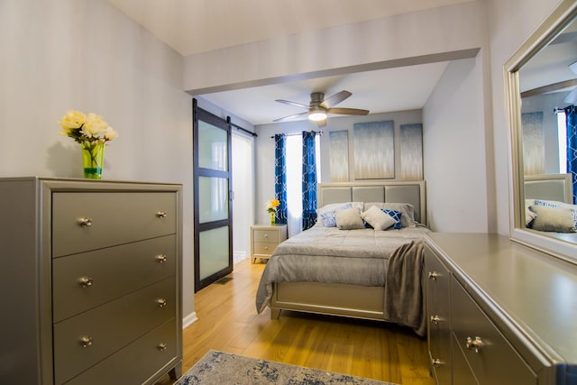 bedroom featuring a barn door, light hardwood / wood-style flooring, and ceiling fan