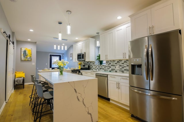 kitchen with a barn door, white cabinetry, and appliances with stainless steel finishes