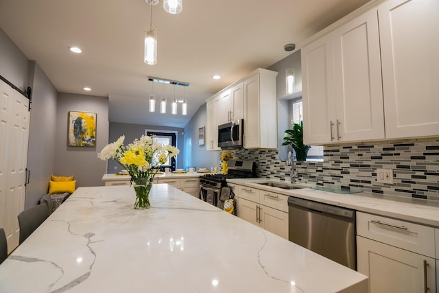 kitchen with light stone counters, stainless steel appliances, a barn door, white cabinetry, and hanging light fixtures