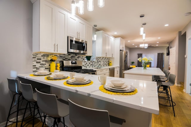 kitchen with a breakfast bar area, white cabinets, stainless steel appliances, and light hardwood / wood-style floors