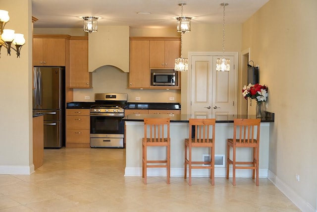 kitchen with light brown cabinets, pendant lighting, stainless steel appliances, and a breakfast bar area