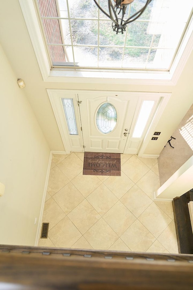 tiled foyer entrance featuring ornamental molding and a chandelier