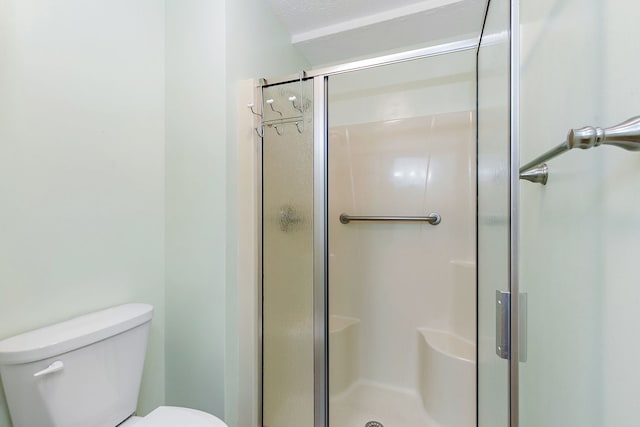 bathroom with a textured ceiling, toilet, and a shower with door