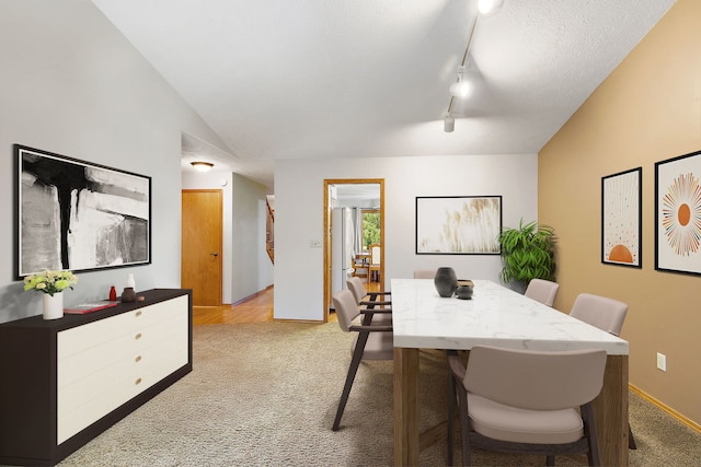 dining area featuring light carpet, a textured ceiling, rail lighting, and lofted ceiling