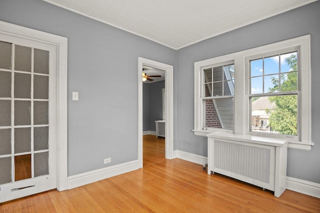 unfurnished room with ceiling fan, light wood-type flooring, and radiator heating unit