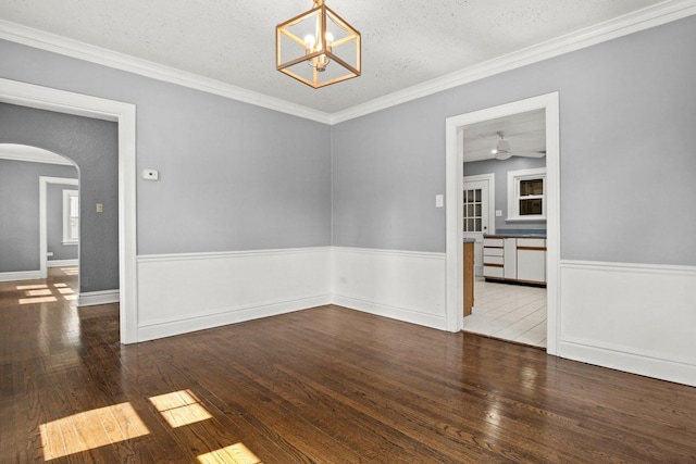 empty room with a textured ceiling, dark wood-type flooring, crown molding, and a chandelier