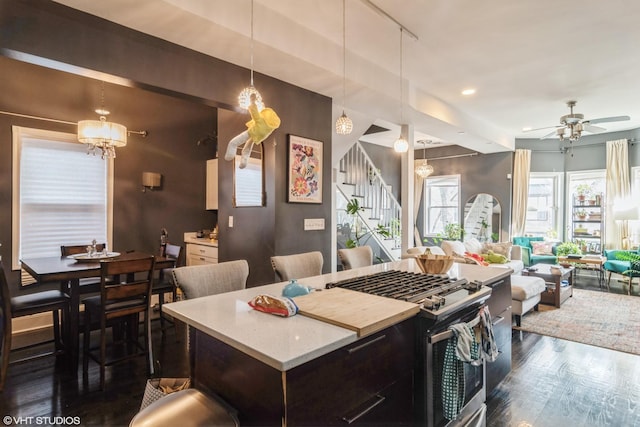 kitchen featuring stainless steel range with gas stovetop, ceiling fan, dark hardwood / wood-style flooring, hanging light fixtures, and a kitchen island