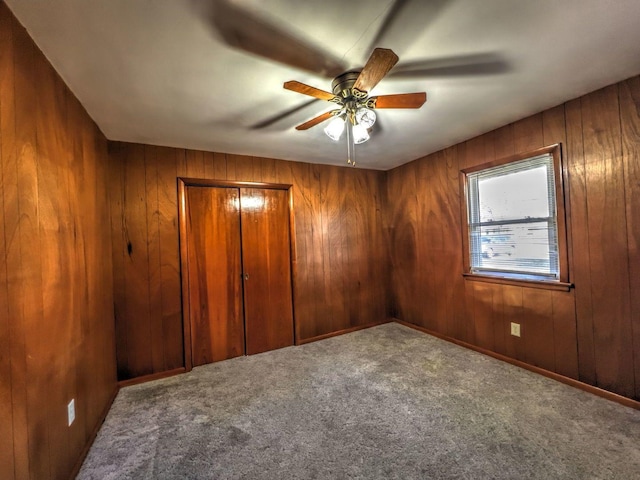 carpeted empty room with ceiling fan and wood walls