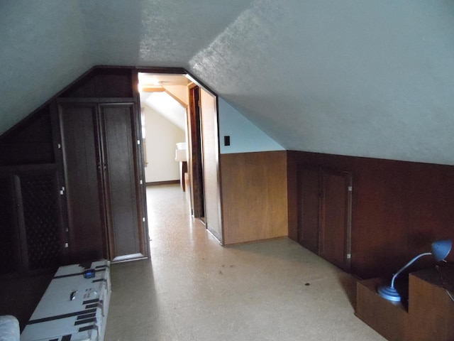 additional living space with a textured ceiling, wooden walls, and vaulted ceiling