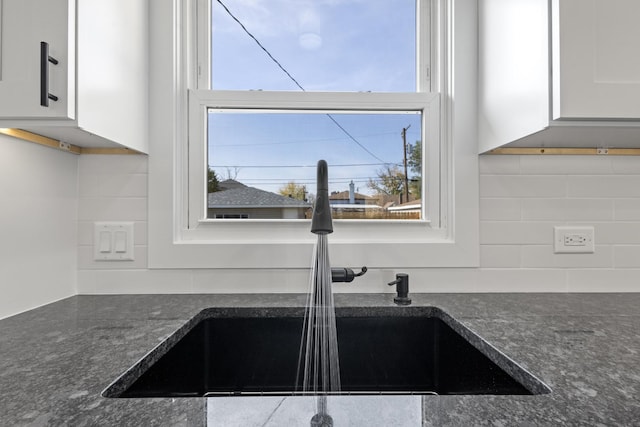 kitchen featuring decorative backsplash, dark stone countertops, white cabinetry, and sink