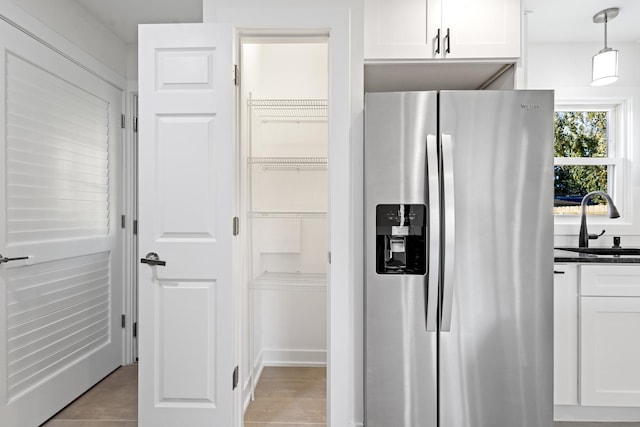 kitchen with sink, light tile patterned floors, stainless steel refrigerator with ice dispenser, decorative light fixtures, and white cabinets