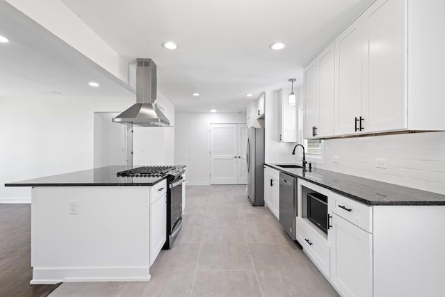 kitchen with stainless steel appliances, wall chimney range hood, a kitchen island, dark stone countertops, and white cabinets