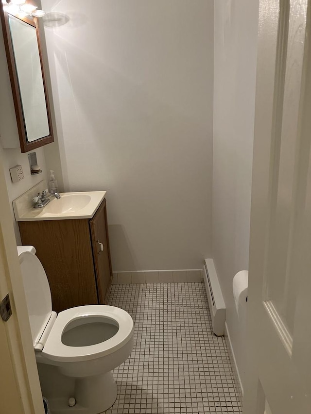 half bath with a baseboard radiator, tile patterned flooring, toilet, vanity, and baseboards