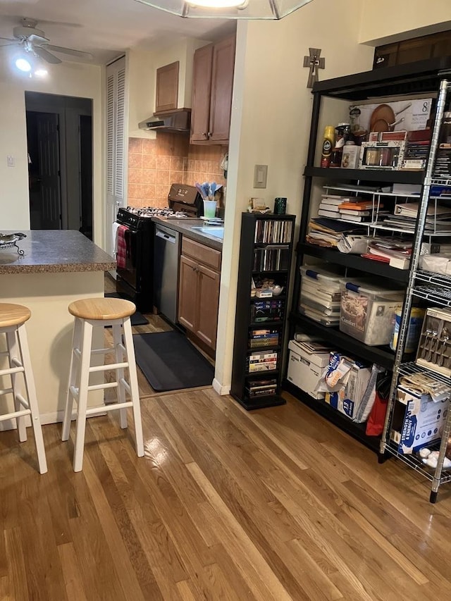 kitchen featuring decorative backsplash, a breakfast bar, gas stove, dishwasher, and hardwood / wood-style floors