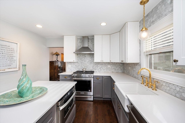 kitchen with stainless steel appliances, dark wood-type flooring, wall chimney range hood, decorative light fixtures, and white cabinets