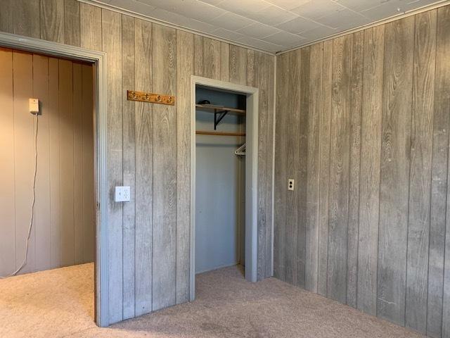 unfurnished bedroom with light carpet, a closet, and wood walls