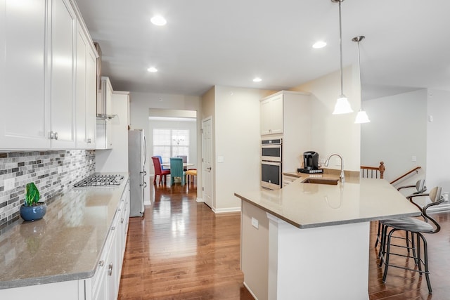 kitchen featuring white cabinets, stainless steel appliances, a breakfast bar, sink, and decorative light fixtures