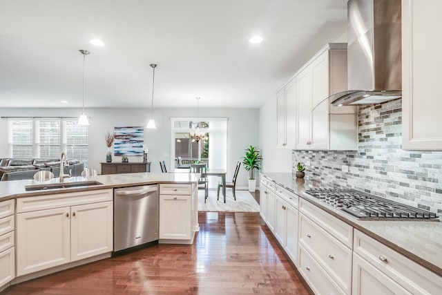 kitchen featuring stainless steel appliances, sink, wall chimney exhaust hood, tasteful backsplash, and pendant lighting