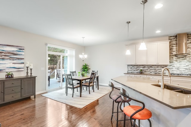 kitchen featuring a breakfast bar area, hanging light fixtures, sink, white cabinetry, and wall chimney range hood